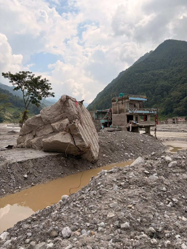Rocher charrié par la crue devant des maisons endommagées